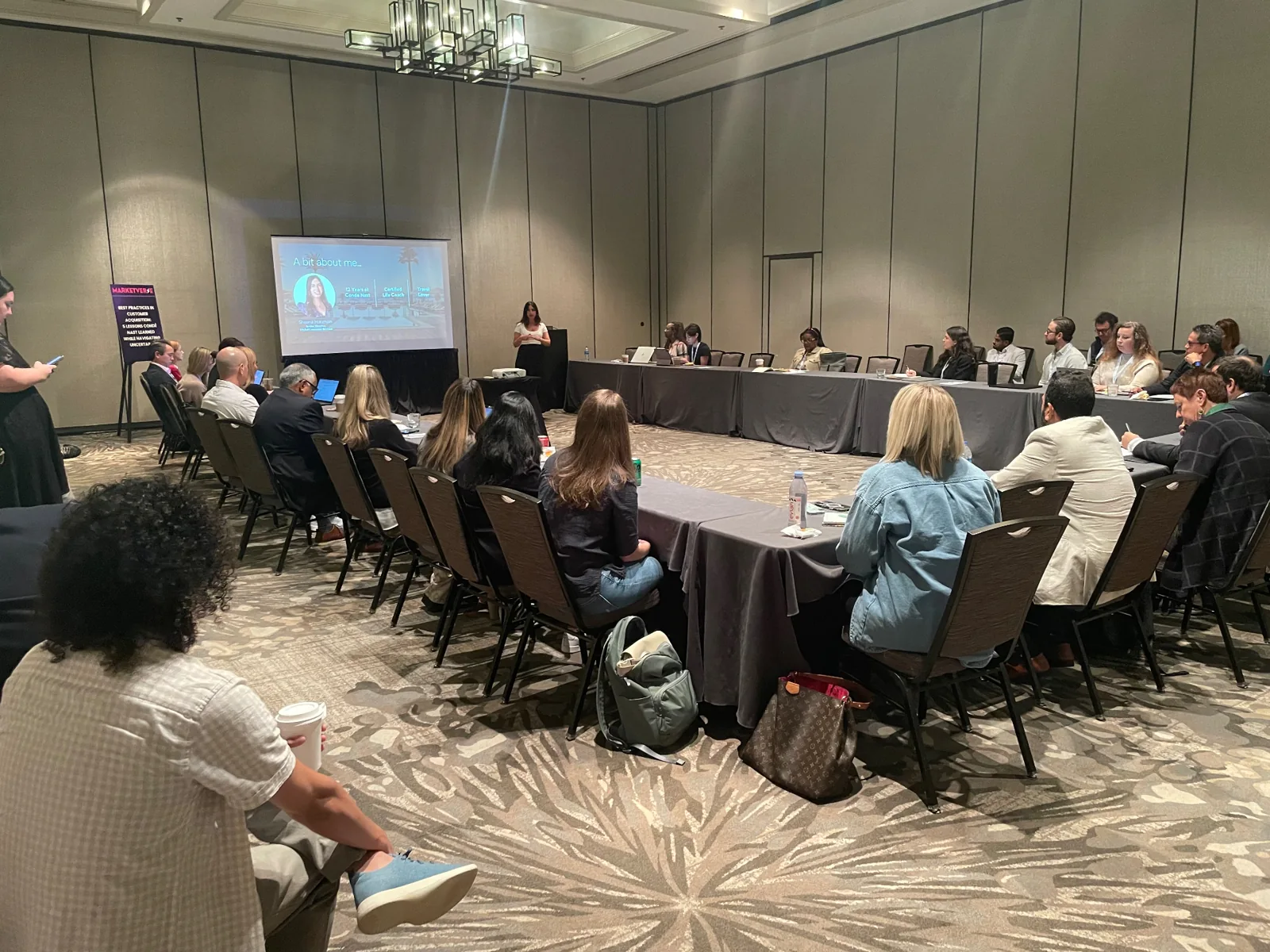 Attendees at an in-person presentation seated around tables